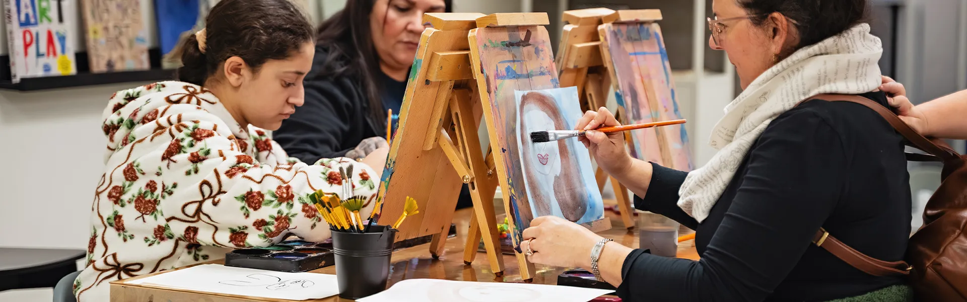 Three people focused on painting portraits on easels in the idea Studio.
